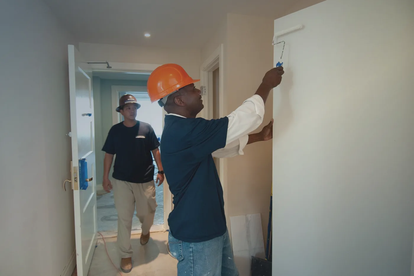 A painter in a hard hat rolling a finish coat onto an interior wall